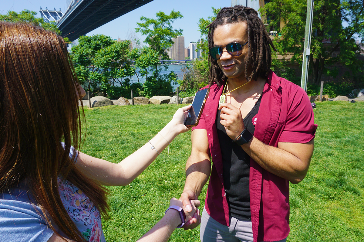 A man holding his QR jumptag necklace while shaking hands with a woman scanning his necklace with her smartphone